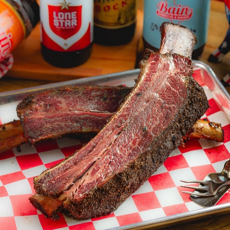 close up photo of medium rare ribs on a checkered paper on pan next to sauce